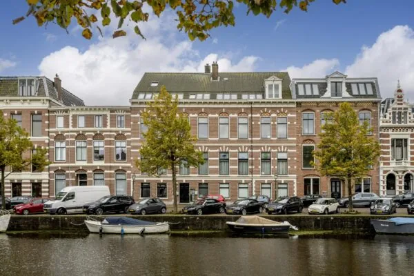Rij monumentale herenhuizen aan de Nieuwe Gracht in Utrecht, met geparkeerde auto's en boten langs het water.